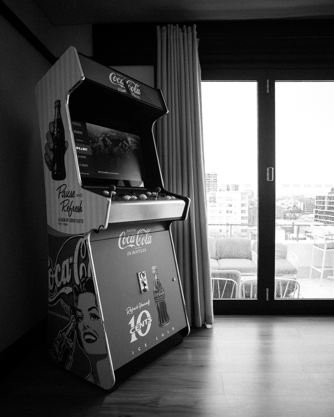 Black and white Coca-Cola arcade cabinet beside the balcony doors