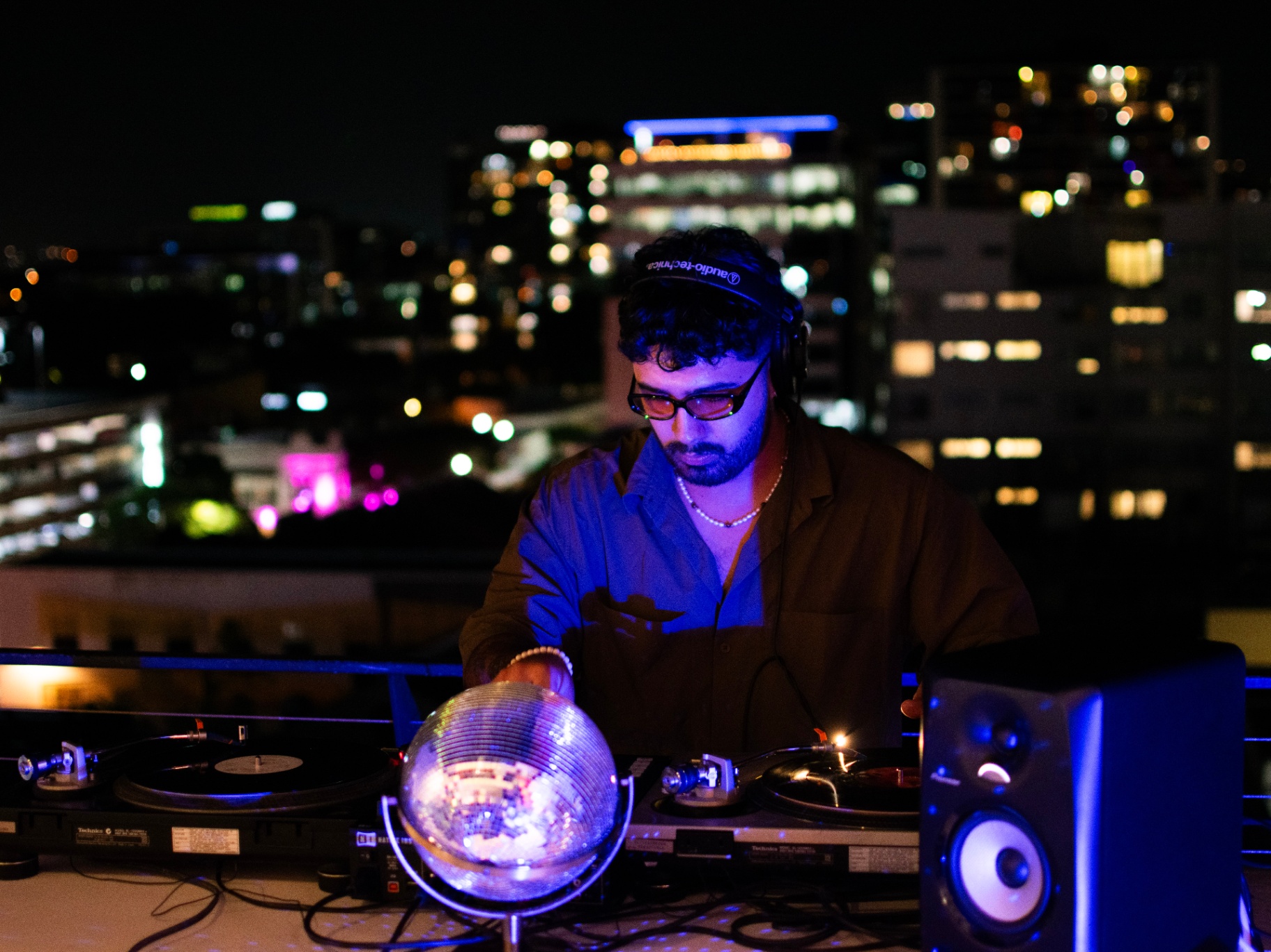 DJ on the rooftop with disco ball and city skyline at night
