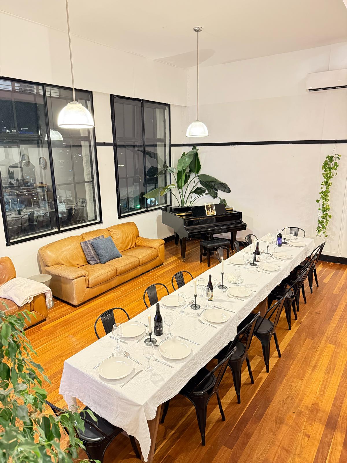 Long dining table set for sixteen with candles, leather sofas and the grand piano behind