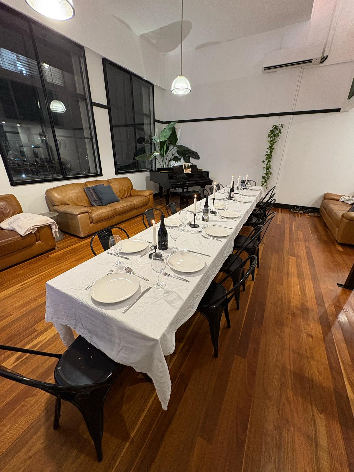 Candlelit long table dressed end-to-end, wine open, the heritage windows behind